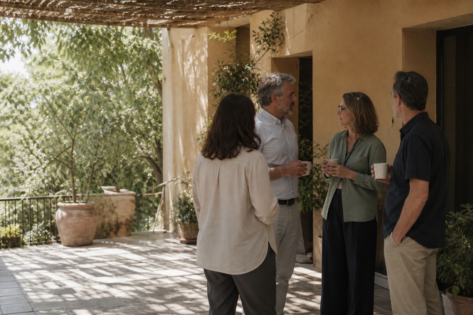 Four practitioners standing and talking together over coffee on a shaded terrace