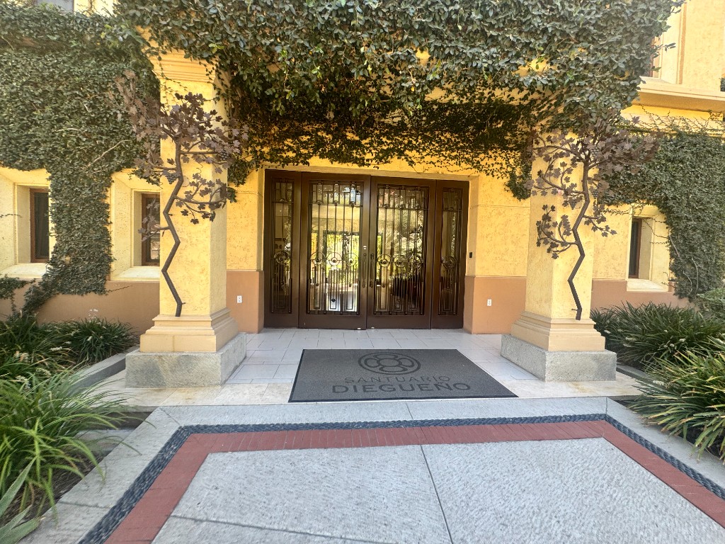 The entrance to Santuario Diegueño: glass doors under ivy, ochre pillars, and a mat with the interlocking-circle mark